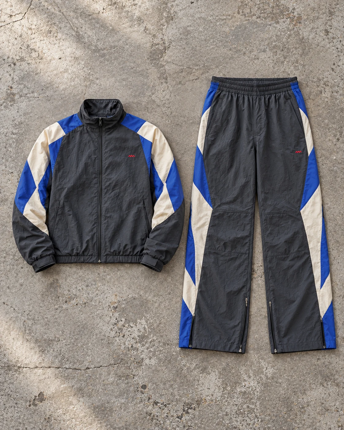 Complete top and bottom flat-lay showing their proportions — Color-Block Woven Tracksuit in charcoal / cobalt / bone, AI-generated design concept