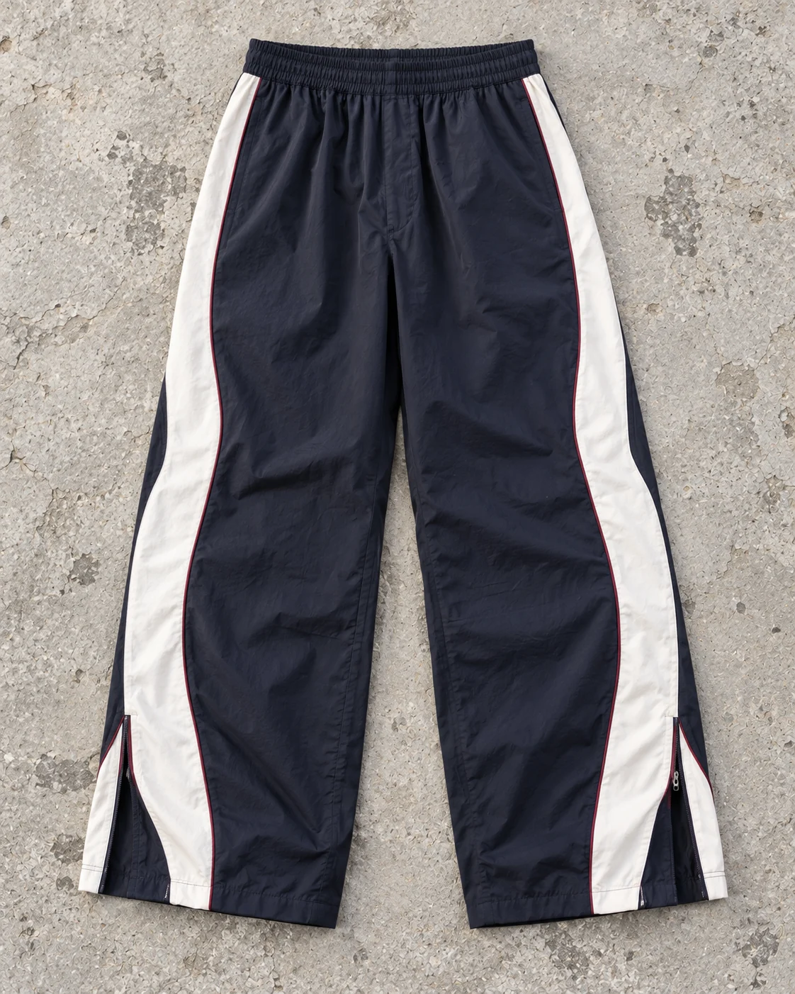 Full garment flat-lay showing the cut — Panelled Track Pants in midnight navy / ivory / burgundy, AI-generated design concept