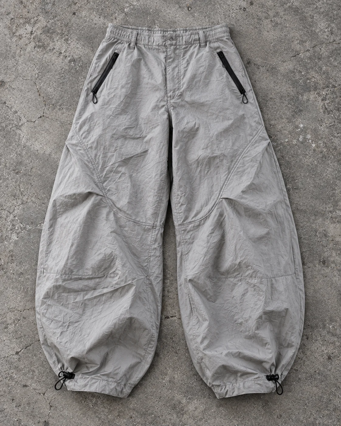 Full garment flat-lay showing the cut — Parachute Pants in stone grey / charcoal, AI-generated design concept